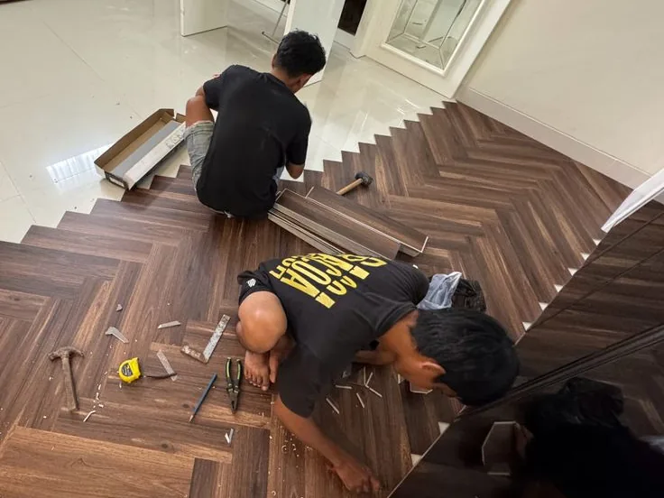 Dua tukang ASATURA memasang lantai vinyl motif kayu pola herringbone di Jakarta