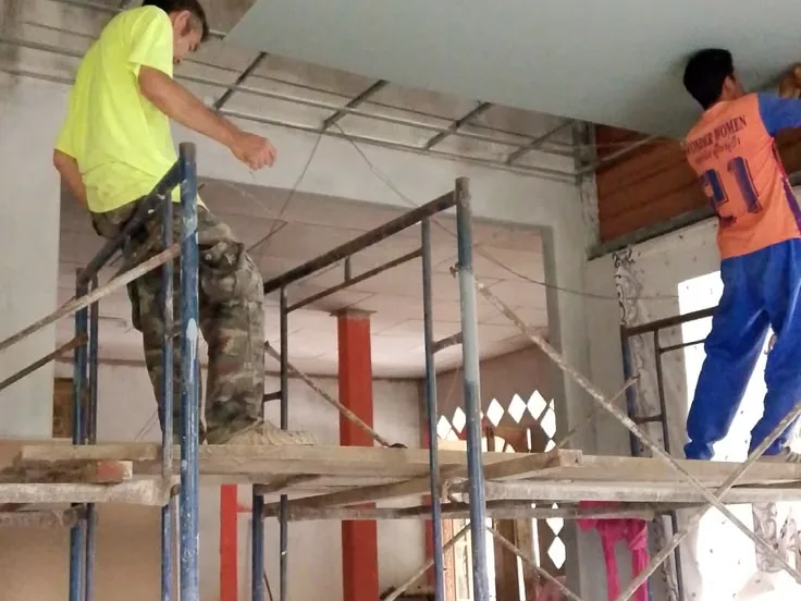 Dua tukang ASATURA memasang panel plafon gypsum dari perancah di Jakarta